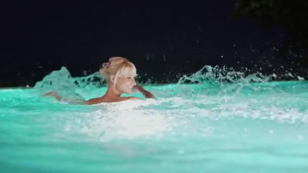 Mujer rubia sonriente salpicando en una piscina — Vídeo de stock