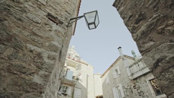Úchvatný pohled na ulici ve starém městě Ulcinj při západu slunce. Květináče s květinami stojící na dlážděném chodníku podél kamenné zdi. Sluneční světlo na kamenném oblouku. Cestování Černou Horou — Stock video