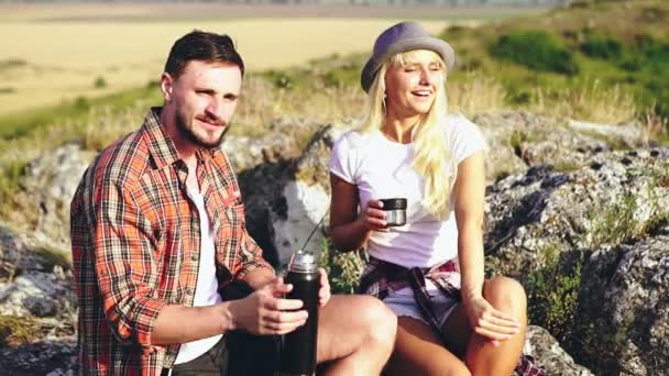 Egy fiatal nő kávét iszik és a barátjával pihen túrázás közben. Két fiatal barát kirándulás közben szünetet tart.. — Stock videók