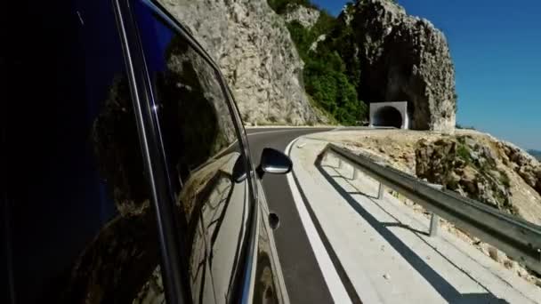 Modern car riding on asphalt road near mountain and then entering tunnel during trip on sunny day in countryside of Montenegro. — Stock Video