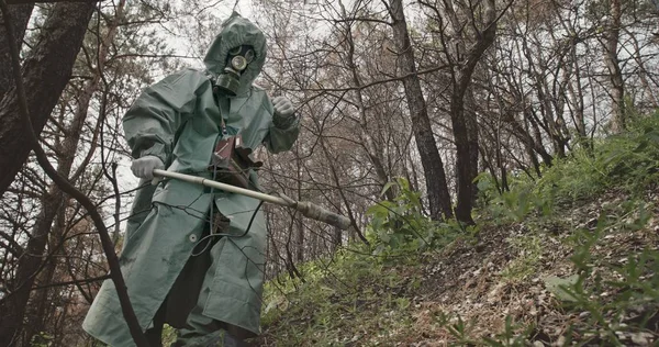 Låg vinkel oigenkännlig kille i Hazmat kostym och gasmask söka efter strålning med geigermätare i övergivna skogen nära Tjernobyl. — Stockfoto