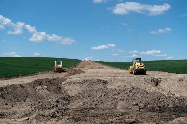 İki buldozer yeşil arazide bir yol inşa ediyor.