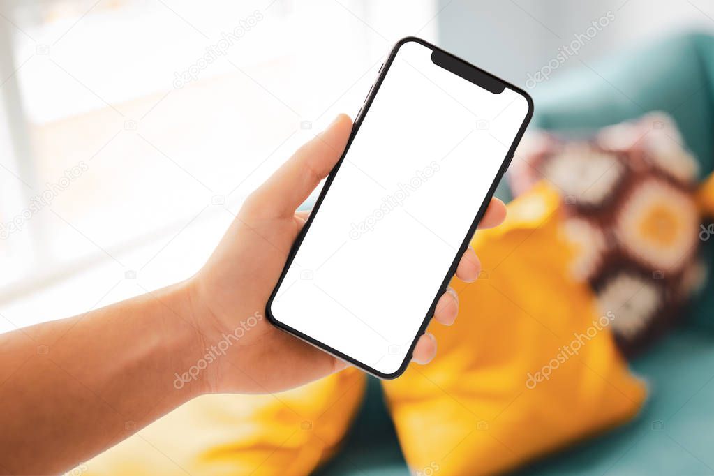 Man hand holding the black smartphone with big blank screen and modern frame less design in home interior, living room - isolated on white background angled position