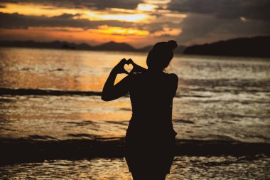 Kız denizde batan güneşin arka plan üzerinde bir kalp şekil verme