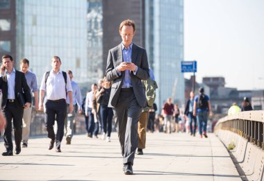 Londra, Ingiltere-19 Nisan 2018: ofis çalışanları, Avrupa 'nın önde gelen iş ve finans alanı olan Londra şehrine giden yolda sabah erkenden Londra Köprüsü 'nü geçiyor. Acele saatleri