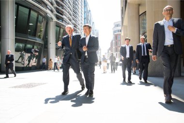 Londra, İngiltere - 26 Haziran 2018: Güneş ışığına karşı şehirde yürüyen bir grup iş adamı. Güzel güneş tarafından sokak aydınlatılmış, City of London modern meşgul kavramı.