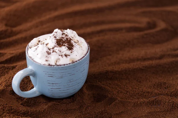 Nahaufnahme von leckerem Kaffee und Schlagsahne. Tasse auf einem Tisch mit gemahlenem Kaffee bedeckt — Stockfoto