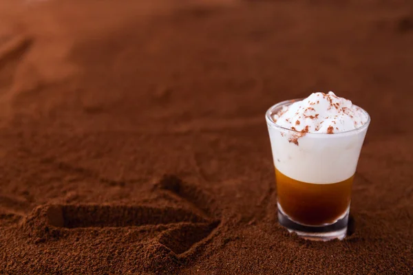 Kleine Tasse Piccolo Latte Macchiato auf einem Tisch mit Pfeil auf gemahlenem Kaffee als Hintergrund bedeckt — Stockfoto
