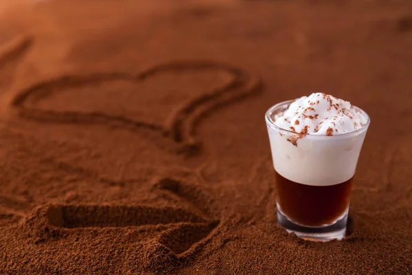Kleine Tasse Piccolo Latte Macchiato auf einem Tisch mit Herz und Pfeil auf gemahlenem Kaffee als Hintergrund bedeckt — Stockfoto