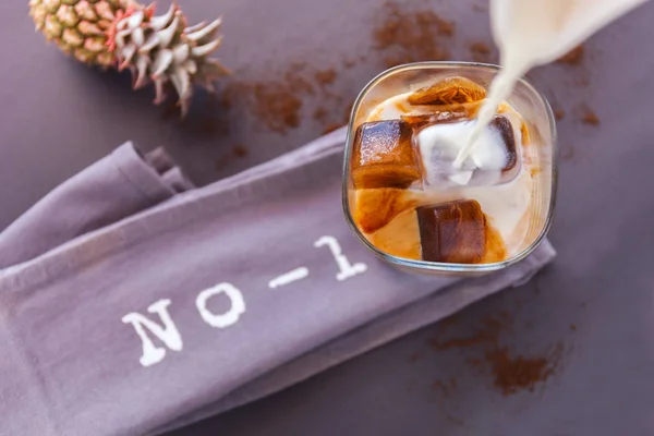 Milch in ein Glas Eiskaffeewürfel auf dunklem Hintergrund gießen. Buchstaben Nummer 1 und Pinapple — Stockfoto