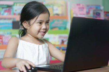 Asyalı çocuk ya da kız çocuğu internetten öğrenim görüyor ya da bilgisayar başında çalışıyor ya da anaokulundan ilkokula kadar dizüstü bilgisayar oynuyor ve Coronavirus covid-19 'dan karantinaya mutlu bir şekilde gülümsüyor.