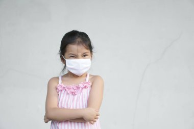 Asyalı çocuk kızgın ya da kız çocuk somurtkan yüz maskesi takıyor. Soğuk algınlığını önlemek için grip virüsü, kovid-19 veya koronavirüs ve başbakteri tozunu dumanla ve çaprazlanmış kollarla korumak için.