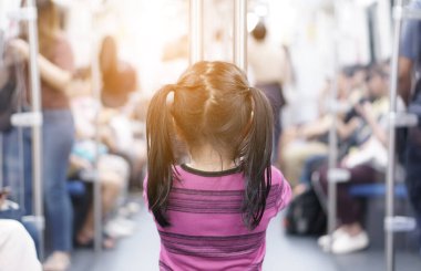 Asyalı bir çocuğun ya da bir kızın arkasında gökyüzü treninin ya da metro rayları ya da metro rayları olan elektrikli trenin arkasında durmanın ve şehir sokaklarında sıcak ışık altında keyifli yolculuklar yapmanın keyfini çıkarın.