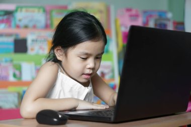 Asyalı çocuk ya da kız çocuğu internetten öğrenim görüyor ya da bilgisayarla bilgisayar başında çalışıyor ya da anaokulundan ilköğretime kadar dizüstü bilgisayar iletişimi kuruyor ve Coronavirus covid-19 hastalığından mutlu bir şekilde gülümsüyor.