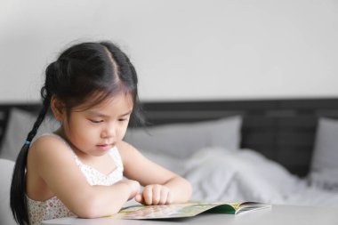 Asyalı çocuk şirin ya da çocuk mutlu ya da öğrenci masal kitabı ya da çizgi film okumaktan zevk alır ve evde, yatak odasında ya da anaokulundaki çocuk yuvasında eğitimle okumayı öğrenmek için gülümser.