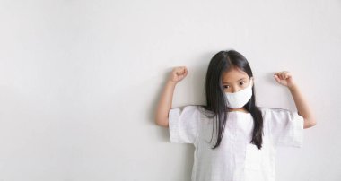 Asyalı çocuk sağlıklı ya da çocuk güçlü bir bez yüz maskesi takıyor. Ağzı kapalı ve soğuk öksürük hastalığına yakalanmış ve soluk soluklu virüsü veya beyaz arka planda duman ve kas yumruğuyla PM2.5 tozunu koruyor.