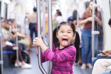 Asyalı şirin çocuk ya da kız çocuk dillerini uzatır gökyüzü treninde ya da metro ya da metro raylı elektrikli trende eğlenir ve şehir sokaklarında mutlu seyahat ya da ulaşım için tırabzan tutar.