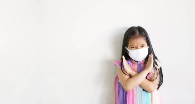 Asyalı çocuk çapraz kolu ya da çocuk güçlü N95 kağıt yüz maskesi takar ve soğuk öksürükle mücadele eder ve PM2.5 tozu veya grip virüsü ile bakterileri beyaz uzayda dumandan korur.