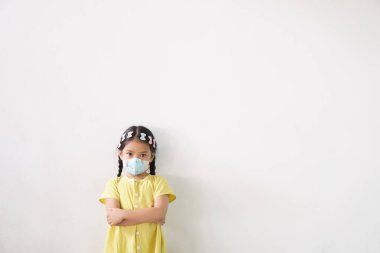 Asyalı çocuk ya da çocuk ağzı kapalı olarak N95 kağıt maskesi takıyor ve soğuk öksürükle burun üstü hasta ve PM2.5 tozu veya grip virüsünü ve bakterileri beyaz arka planda çaprazlanmış duman ve kollardan koruyor.