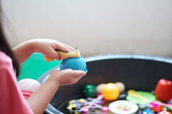 closeup hand of child or kid girl wash and cleaning colorful plastic toy in water basin black by sponge for kill bacteria or dirty disease and dust sterilize from coronavirus covid-19