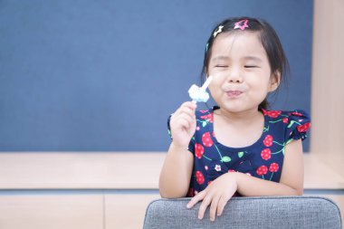 Asyalı çocuk ya da kız çocuk gülümser ve tatlı tatlı olarak çilekli dondurma ve yaz mevsiminde aşırı hassas dişler ve anaokulunda ya da anaokulunda diş hekimliğinde mavi tahta yemekten zevk alır.