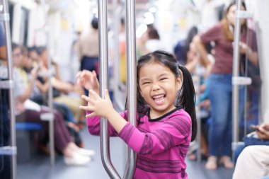 Asyalı şirin çocuk ya da gülümseyen çocuk gökyüzü treninin ya da metrosu olan elektrikli trenin keyfini çıkarın ve şehir sokaklarında mutlu seyahat ya da ulaşım eğlencesi için demiryolu tutun.