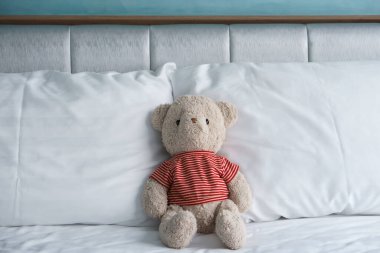 Oyuncak ayı beyaz yatağa ve yatak odasındaki çift yastıklı yastığa oturur. Eski mavi duvar arka planında. Hediye oyuncağı ve sürpriz kış Noel 'inde ya da çocuk ve çocuğun doğum gününde.