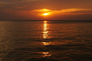 Deniz ve okyanusta gün batımı ya da gün doğumu. Altından gökyüzü ya da alacakaranlıkta kırmızı ve turuncu güneş ışığı. Su ve bulutun yansımasıyla manzara sahnesi ve doğa gecesi manzarası veya yaz arkaplanı.