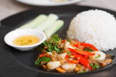 Öğle yemeği için acılı balık soslu siyah tabakta salatalık ve beyaz pirinçle karışık fesleğen ya da restoranda ya da yemek salonunda Tayland deniz ürünleri karıştırın.