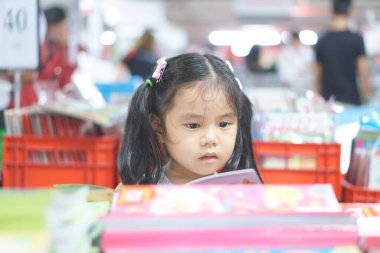 Anaokulundaki ya da anaokulundaki kütüphanedeki kitaplıkta ya da çocuk yuvasında öğrenim görmek için okuduğu çocuk yuvasında ya da çocuk yuvasında mutlu bir şekilde alışveriş yapmaktan ve hikaye veya hikaye kitaplığından kitap seçmekten zevk alır.