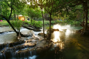 camping tent on stream and waterfall with tree in green jungle or forest for summer holiday relax and vacation travel trip with trekking and picnic on meadow or grass at Huai Mae Khamin Waterfall clipart