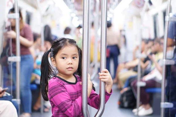 Asian child cute or kid girl smiling enjoy in bogey of sky train or electric train with underground railways or subway and holding rail for happy travel or transportation fun in city street on holiday