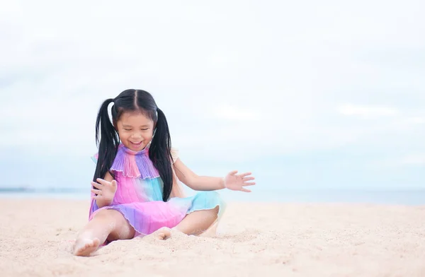 asian child cute or kid girl happy enjoy and sit on sea beach with playing white sand and laugh or smiling cheerful on summer holiday relax and vacation travel with wear colorful dress and fun