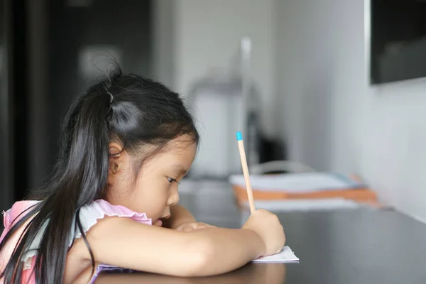 アジアの子供は可愛くて子供は笑顔勤勉な書き込みや絵を描き 教室のテーブルの上で白い紙や保育園や幼稚園の本で宿題や幸せな学習や訓練を行うことを楽しむ — ストック写真