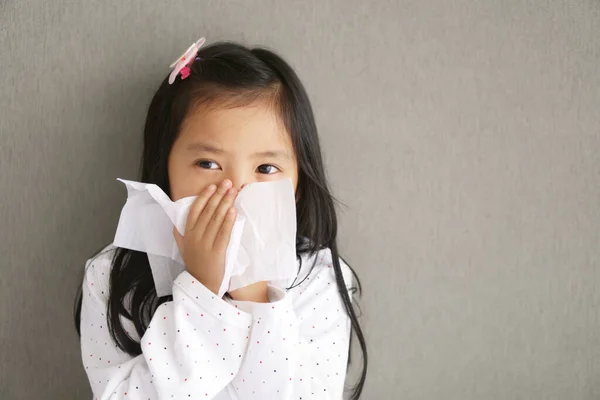 Asian child or kid girl sick and sad with sneezing on nose and cold cough on tissue paper because influenza and allergy weak or virus bacteria from dust weather or smoke at kindergarten school or home and stay safe from coronavirus covid-19