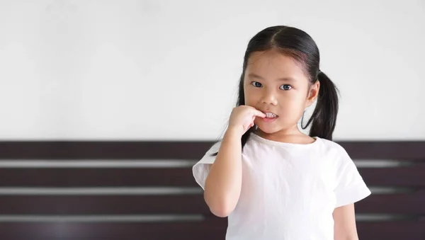 アジアの子供かわいいまたは子供の女の子の爪指にかむと不安や思考で笑顔就学前や5歳でお楽しみくださいコピースペースと白いTシャツを着用 — ストック写真