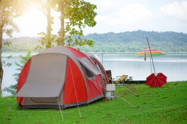nature landscape red camping tent and colorful umbrella under the tree on green grass meadow or park with lake or river and tree mountain jungle for picnic travel on family vacation and holiday relax