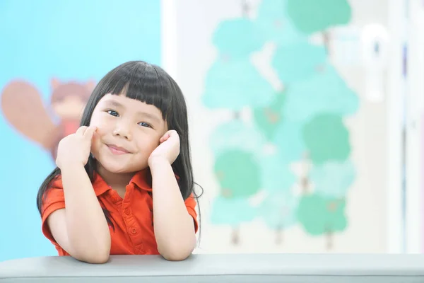 アジアの子供かわいいまたは子供の女の子は 新しいアイデアや創造的な芸術を考えているか 空白で楽しいか 青と白のスペースを持つ幼稚園や保育園や子供病院でソファの上に赤いシャツを着て笑顔 — ストック写真