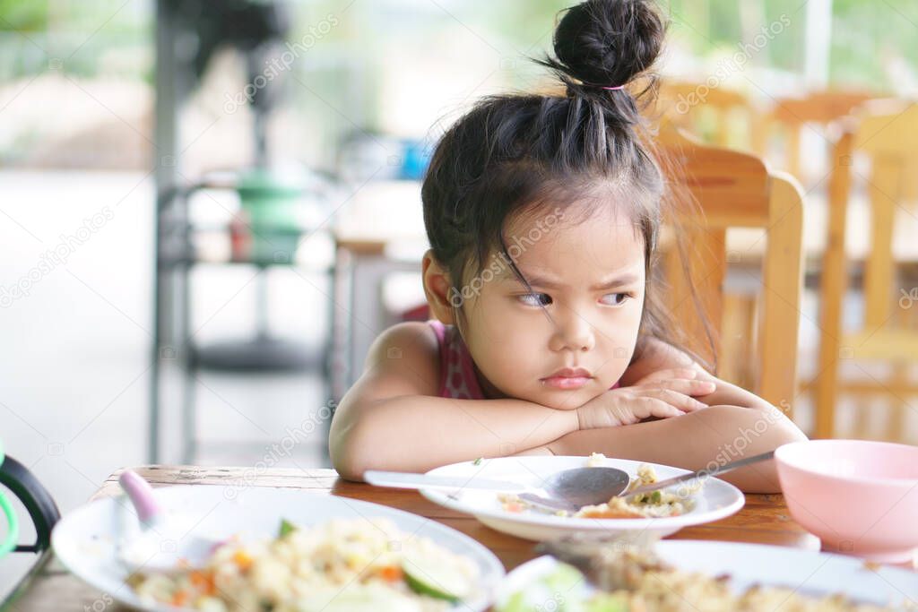 Asian child cute or kid girl anorexia or sad and bored food or boredom with sleepy vacant and prop up or hand to cheek on wood table for breakfast or lunch eating at restaurant on preschool