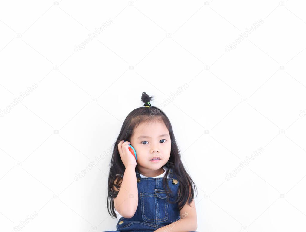 Asian child cute or kid girl smiling and playing smartphone toy or talking on mobile phone for communication learning or call and wear dungarees jean on white background isolated with space