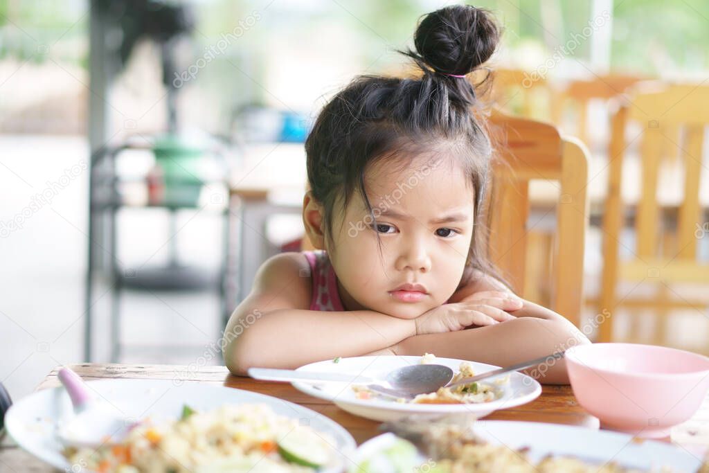 Asian child cute or kid girl anorexia or sad and bored food or boredom with sleepy vacant and prop up or hand to cheek on wood table for breakfast or lunch eating at restaurant on preschool