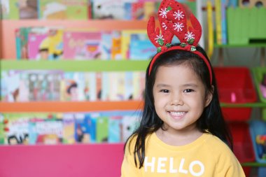 Asyalı çocuk ya da kız çocuk gülümser ve kırmızı boynuzlu ren geyiği saç bandı takar ya da Noel Baba kostümü ya da Noel Baba ya da Noel Baba kostümü giyer ve kış mevsiminde ve raf arka planında eğlenceli yeni yıl festivalleri düzenler.