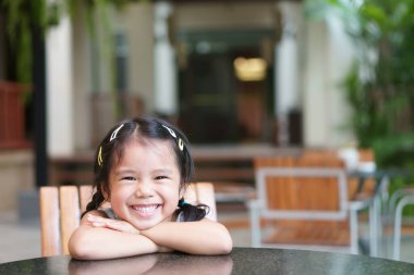 Asyalı çocuk gülüşü ya da çocuk kız öğrenci düşüncesi ya da boş bir fikir ve mutlu eğlence ya da neşe bahçe sınıfında ya da anaokulunda masa ve sandalyeye oturup tatil tatili için dinlenmek.