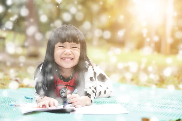 Asian child or kid girl learning for coloring or sleep drawing paint on green mat and nature meadow at autumn garden with funny smile and christmas day snow on winter holiday relax and warm sunlight