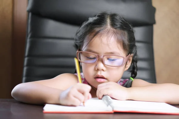 アジアの子供や子供の女の子は 白紙の本や机やテーブルの上で宿題や勉強をしたり 保育園や幼稚園のオフィスで机やテーブルで書くのを楽しむことができます — ストック写真
