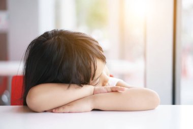 Anaokulundaki beyaz masada dinlenmek için uyuyan ya da uyuyan Asyalı bir çocuk. Çünkü uykulu ya da yalnız anne ve baba sıcak güneş ışığında evde sıkılıyor.