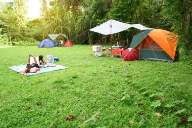Tatil pikniği için orman bahçesinde ya da ormandaki yeşil çimlerin altında tente ve çocuk ailesiyle birlikte doğa kampı çadırı. Tatil seyahatlerinde ya da yaz tatillerinde ya da yağmurlu günlerde dinlenmek için.