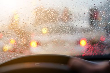 İnsanlar araba aynasında veya ön camında yağmur fırtınası ve trafik sıkışıklığı olan araba ve su damlacıkları kullanıyor. Otoyolda kırmızı ışık altında sıcak güneş ışığı altında arabanın arkasında.