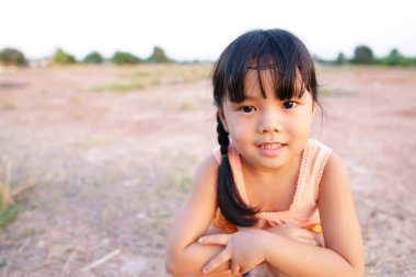 Asyalı çocuklar şirin fakir ya da küçük kızlar neşeli bir şekilde gülümsüyor çünkü memleketlerine dönüp geleneksel bluz ya da kolsuz tişörtler giyiyorlar kurak topraklarda ya da kırsal kesimde tarım için toprak üzerinde oturuyorlar.