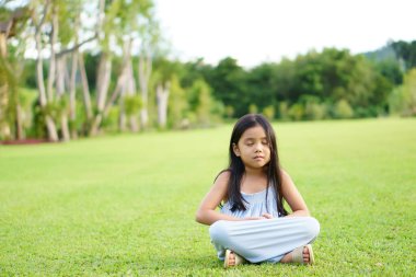 Asyalı çocuk Zen veya çocuk gülümser. Göz teması kurar, derin derin düşünür ve huzur için çimlere ya da çayır çimlerine oturur ya da yoga yapar. Açık tapınak parkındaki ağaç bahçesinde el çakışması ile rahatlar.